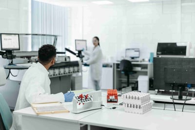 Analytical scientists in a bright lab reviewing racks and documents, illustrating method transfer and lifecycle support across global sites with SOP alignment, comparability, and verification testing.