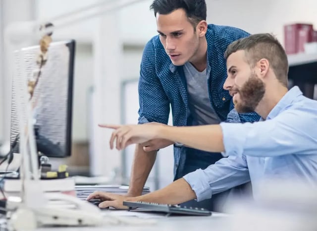 Two colleagues working together at a computer, with one pointing at the screen while discussing project details.