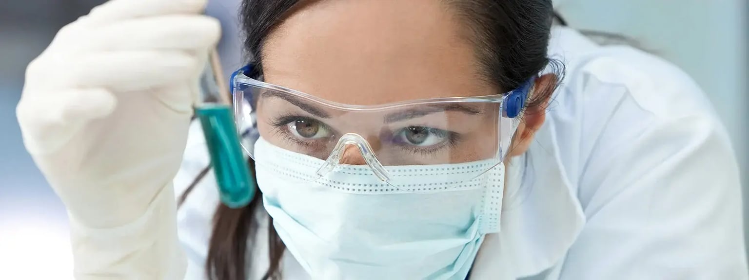 Scientist in PPE wearing safety goggles and a mask examines a pipette sample in a GLP laboratory, representing Crystal Bio Solutions scientific depth and state of the art facilities.