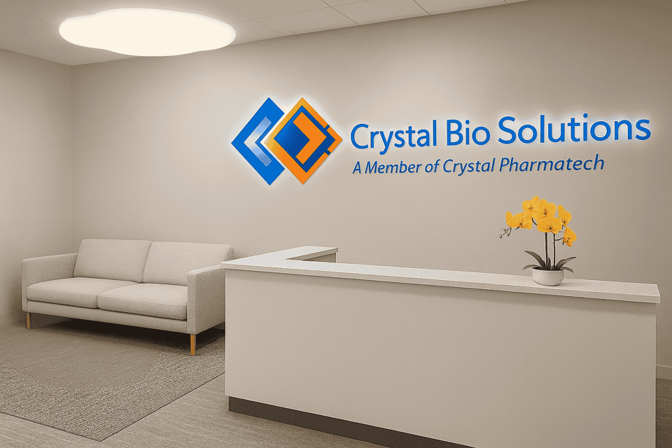 Crystal Bio Solutions reception area with illuminated wall logo, white front desk, sofa, and yellow orchid, representing the company’s headquarters and professional client welcome space.